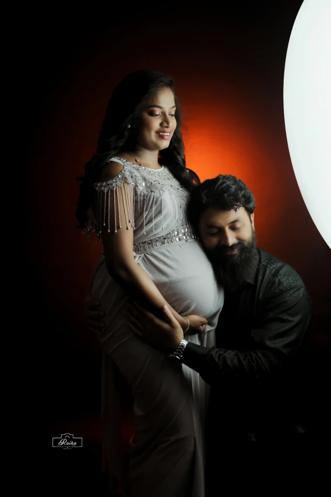 A pregnant woman and man posing in front of a red light.