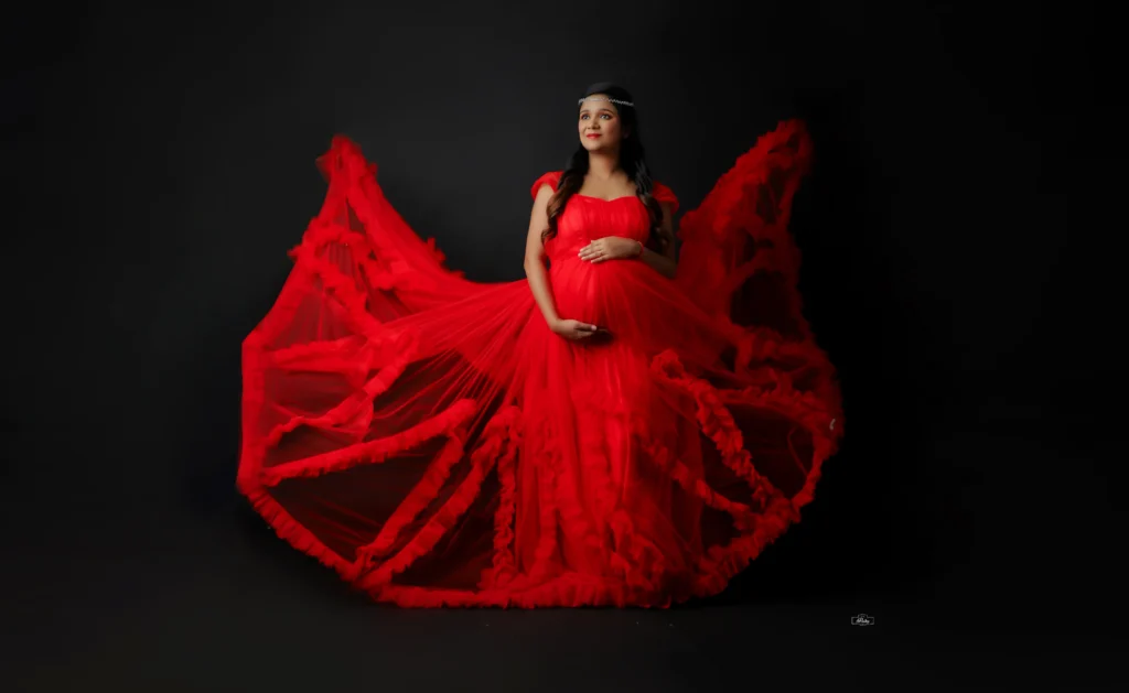A pregnant woman in a red dress posing on a black background.