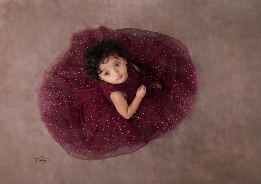 A little girl in a burgundy dress laying on the floor.