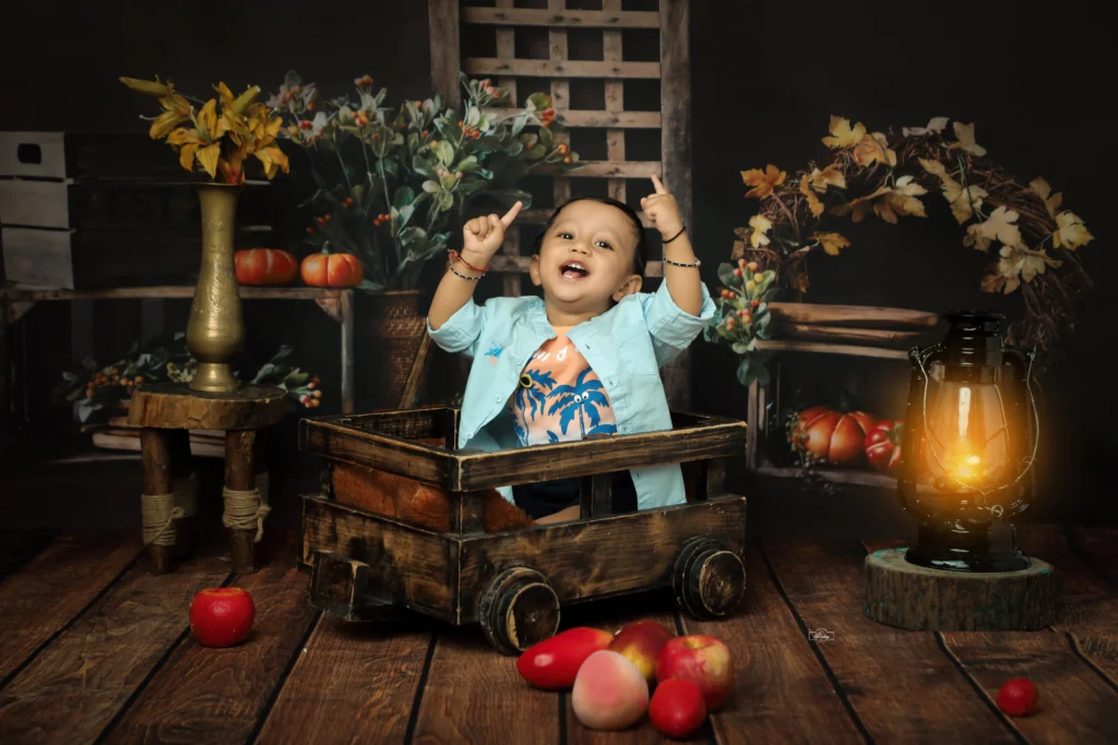 A little boy fun and sitting in a wooden wagon with apples.