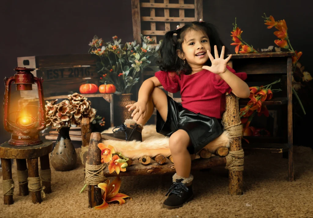 A little girl sitting on a wooden chair in front of a lantern.