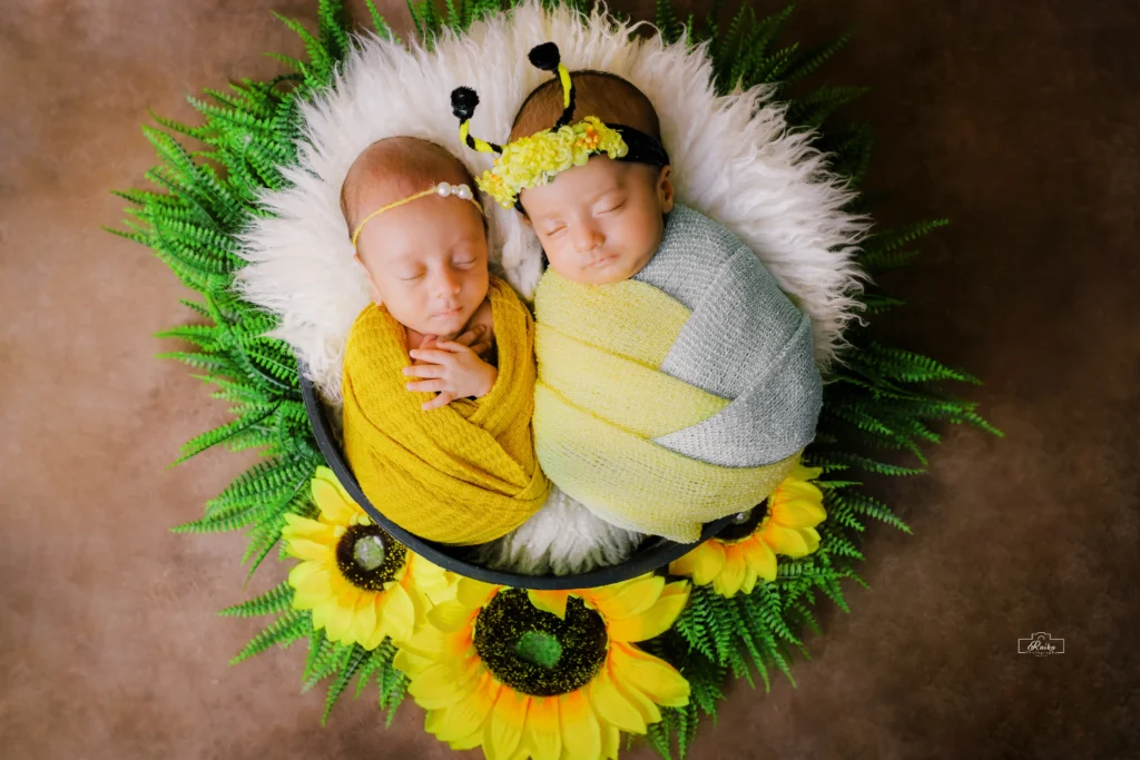 Two newborns wrapped in yellow blankets on sunflowers.